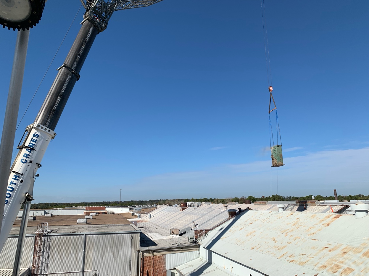 The 400-ton crane lifting the gearbox over the Florida plant rooftop against blue sky