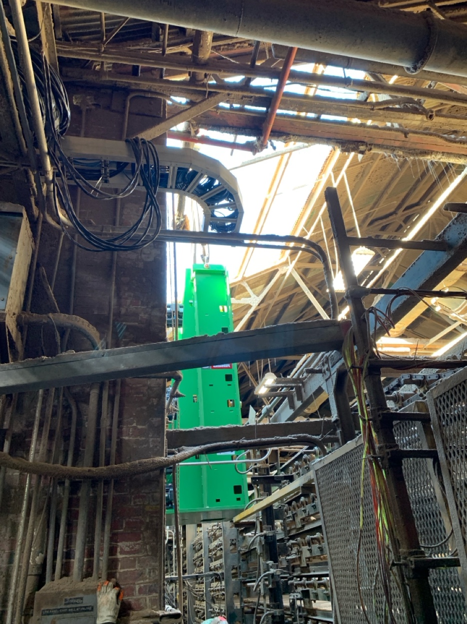 The gearbox suspended inside the plant, visible through layers of industrial infrastructure